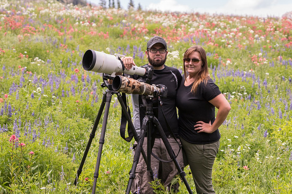 Adam Rice with his wife Kate Rice standing beside photography equipment in a field of wild flowers. Founders of KAR Photography. 