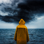A person wearing a yellow rain jacket looks out at the ocean during a rainstorm.