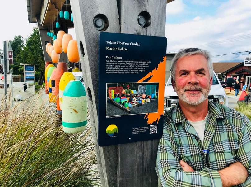 Clarkson standing by the Float'em Garden sign in Tofino, that features his work.