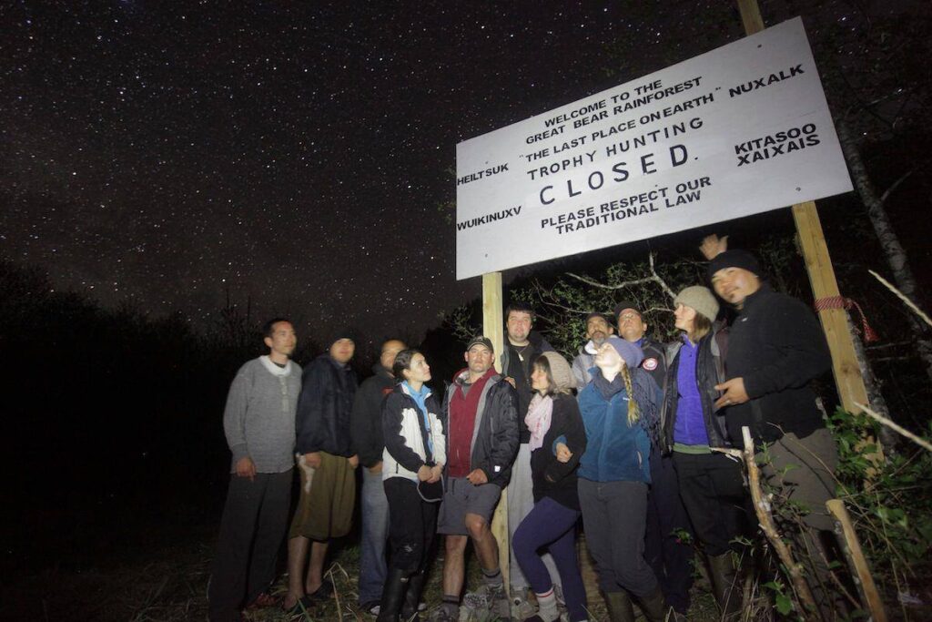 People standing in front of a large sign that says "Welcome to the Great Bear Rainforest". Trophy Hunting Closed.