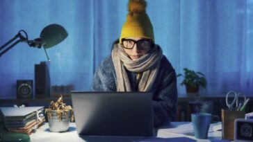 A woman works from home at her computer while wearing winter close.