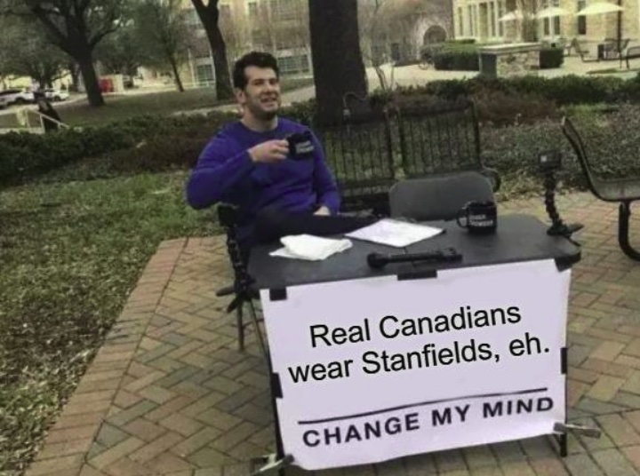 A meme image of a man behind a desk in a park. A sign on the desk says "Real Canadians Wear Stanfields, eh."