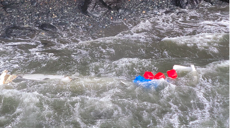 Parts of the wrecked boat floating in the waves near shore.